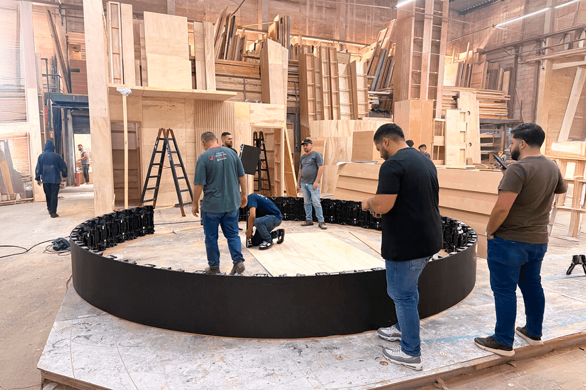 Montagem de Estandes 2 Equipe realiza pré-montagem de estrutura circular sobre piso elevado no galpão de produção de estandes.